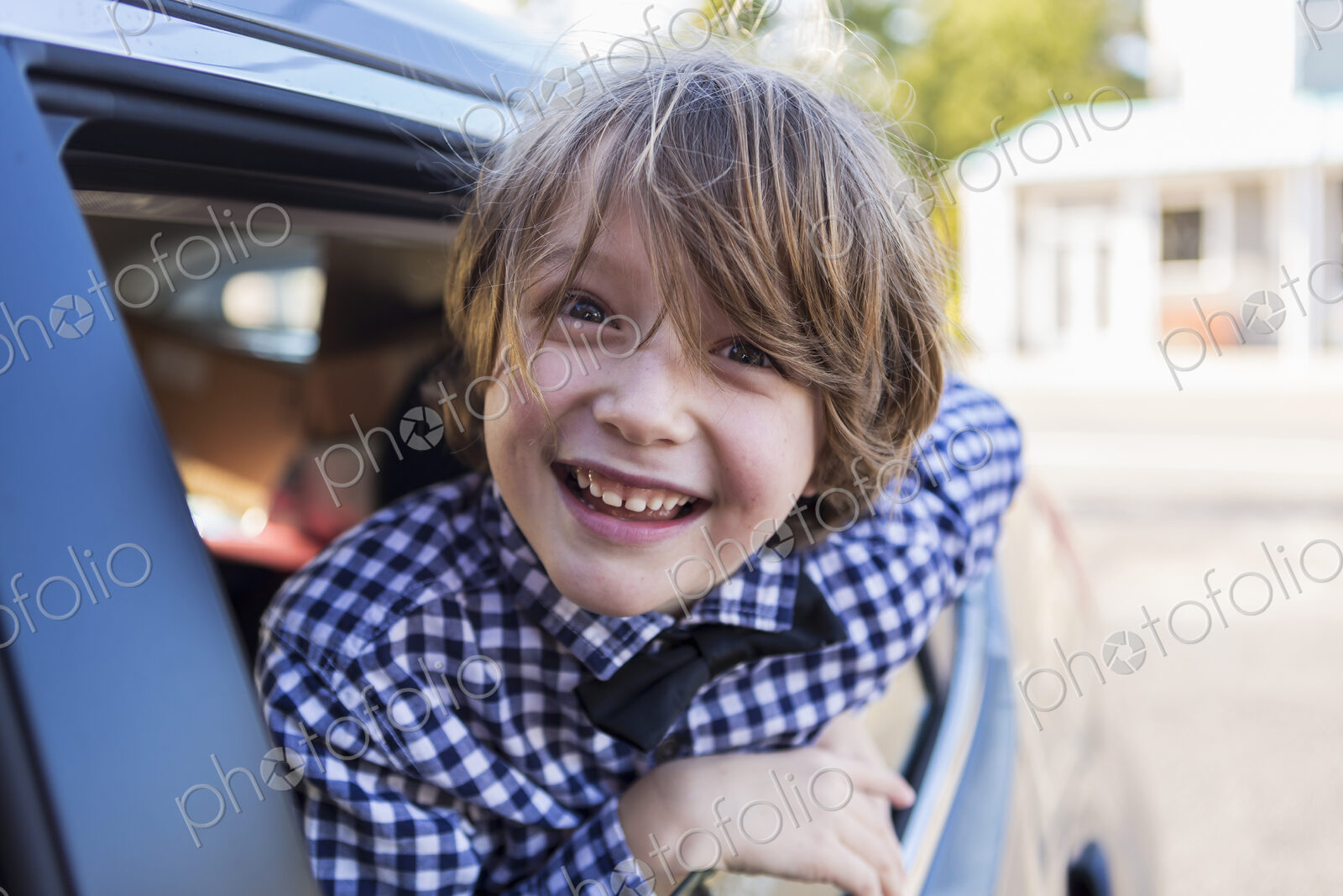 A six year old boy smiling at camera, looking out of car window