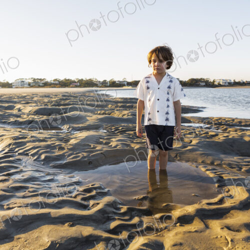 A six year old boy standing in a shallow pool on the sand