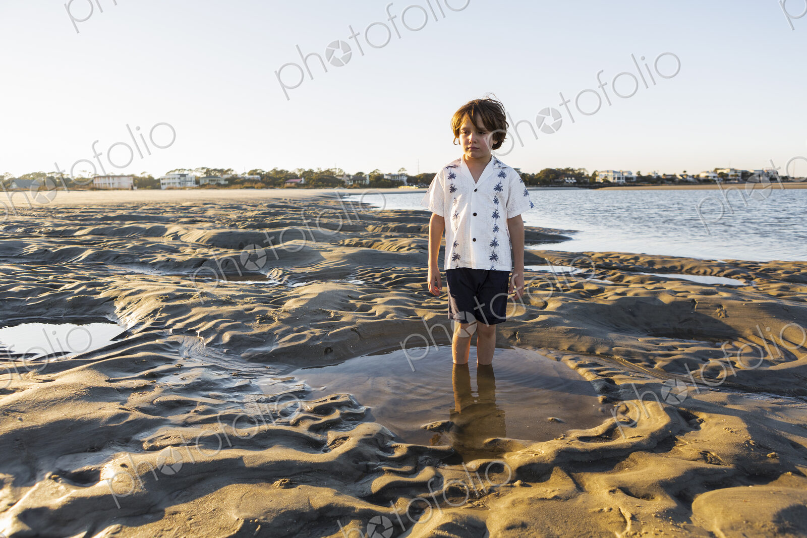 A six year old boy standing in a shallow pool on the sand