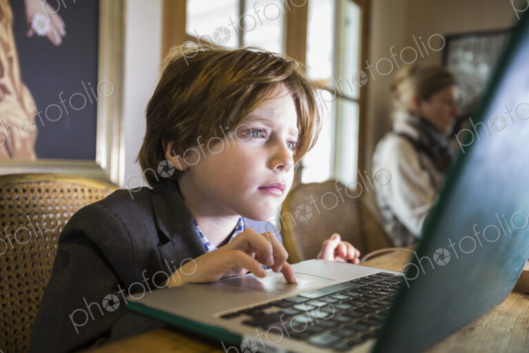A six year old boy typing on a laptop at home