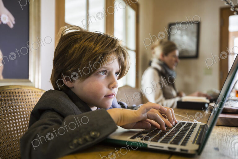 A six year old boy typing on a laptop at home