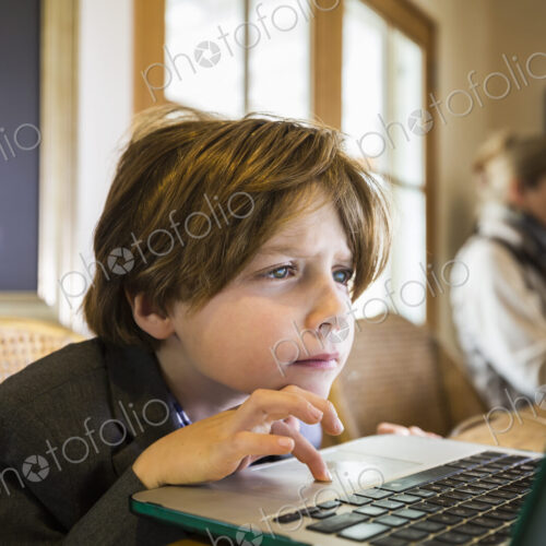 A six year old boy typing on a laptop at home, using the cursor touch pad.