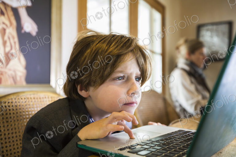 A six year old boy typing on a laptop at home, using the cursor touch pad.
