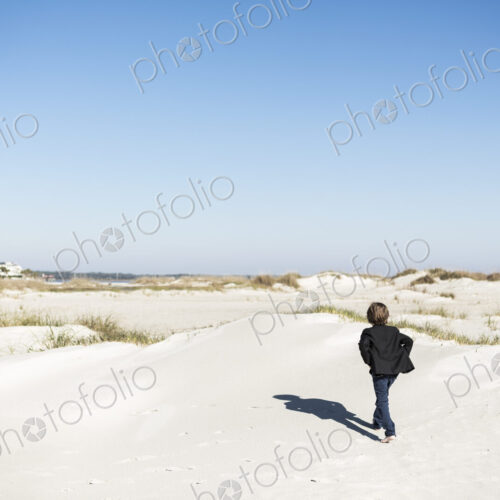 A six year old boy walking over sand dunes in open space. A six year old boy walking over sand dunes in open space.