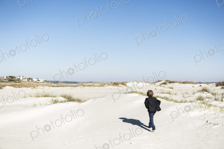 A six year old boy walking over sand dunes in open space.