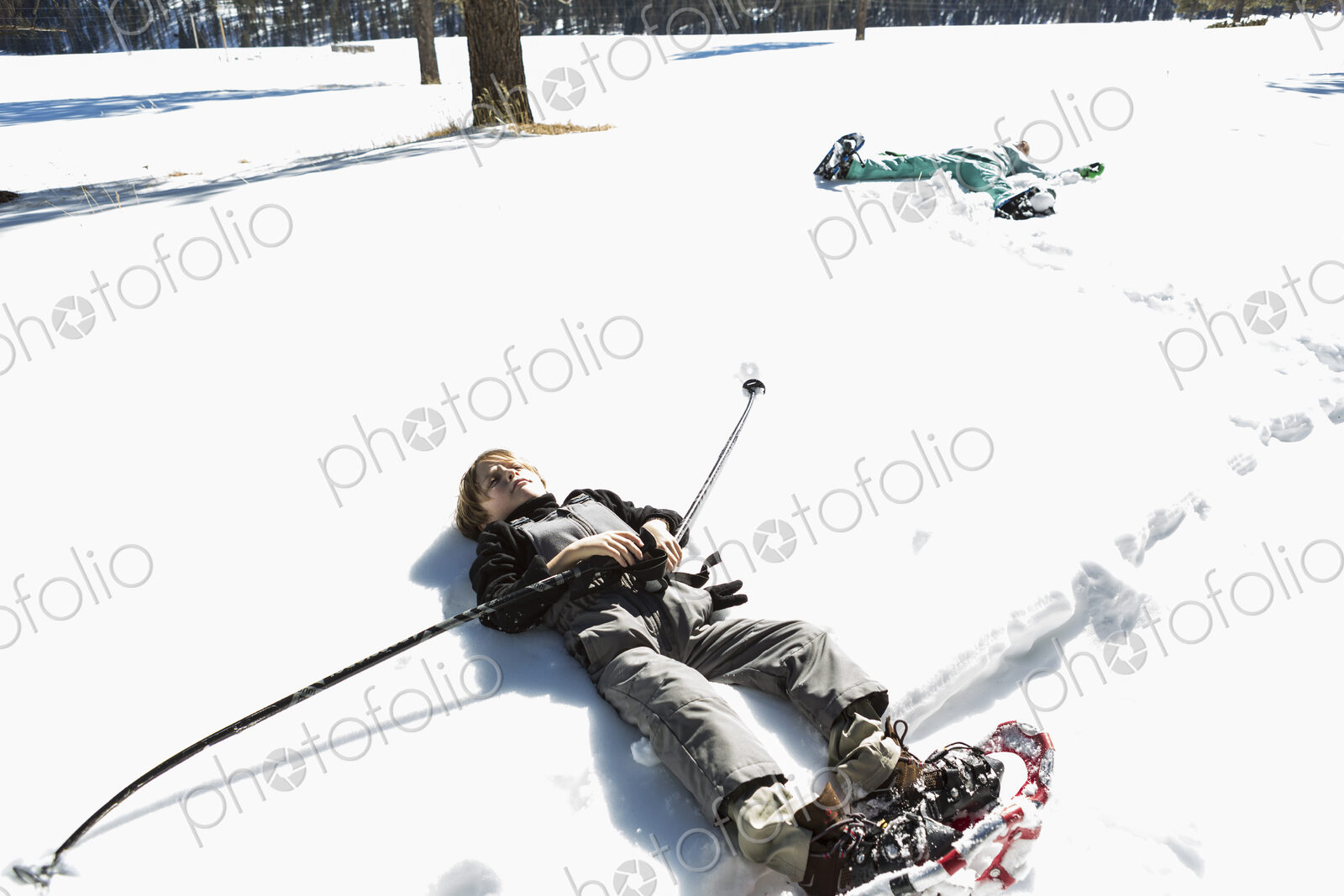 A six year old boy wearing snow shoes, lying down on his back in snow
