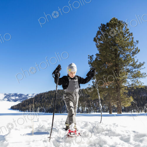 A six year old boy with snow shoes and ski poles
