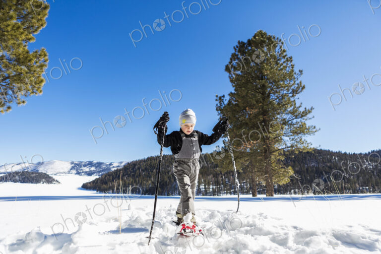 A six year old boy with snow shoes and ski poles