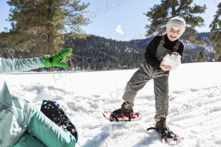 A six year old boy with snow shoes holding a large snowball.