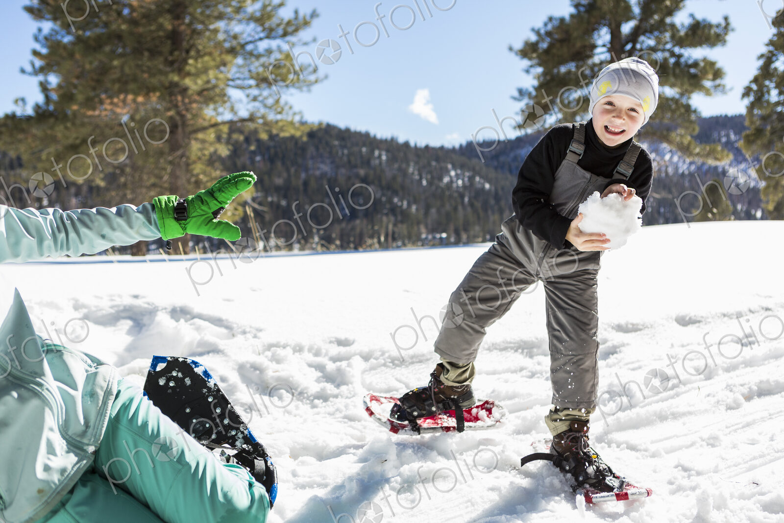 A six year old boy with snow shoes holding a large snowball.