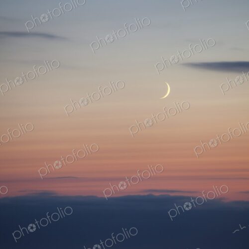 A slender crescent moon rises above the calm Pacific Ocean at dusk, Winchester Bay,… A slender crescent moon rises above the calm Pacific Ocean at dusk, Winchester Bay,…