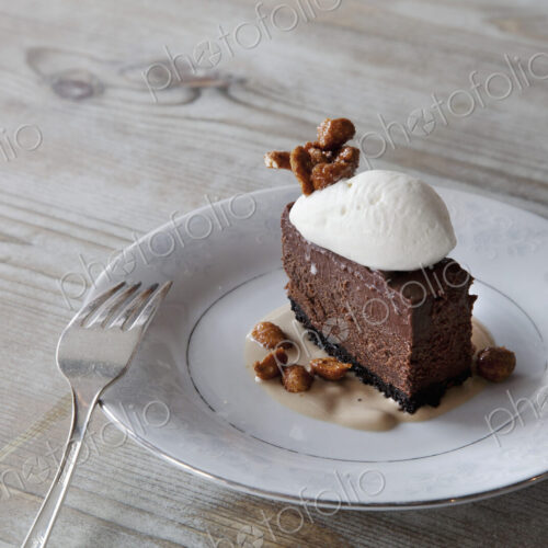 A slice of chocolate mousse dessert with ice cream, nuts nad sauce on a plate.