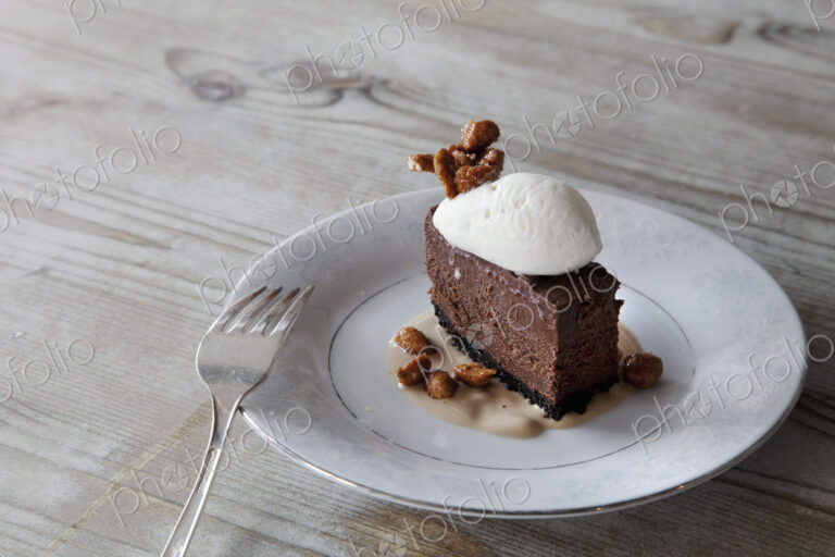 A slice of chocolate mousse dessert with ice cream, nuts nad sauce on a plate.