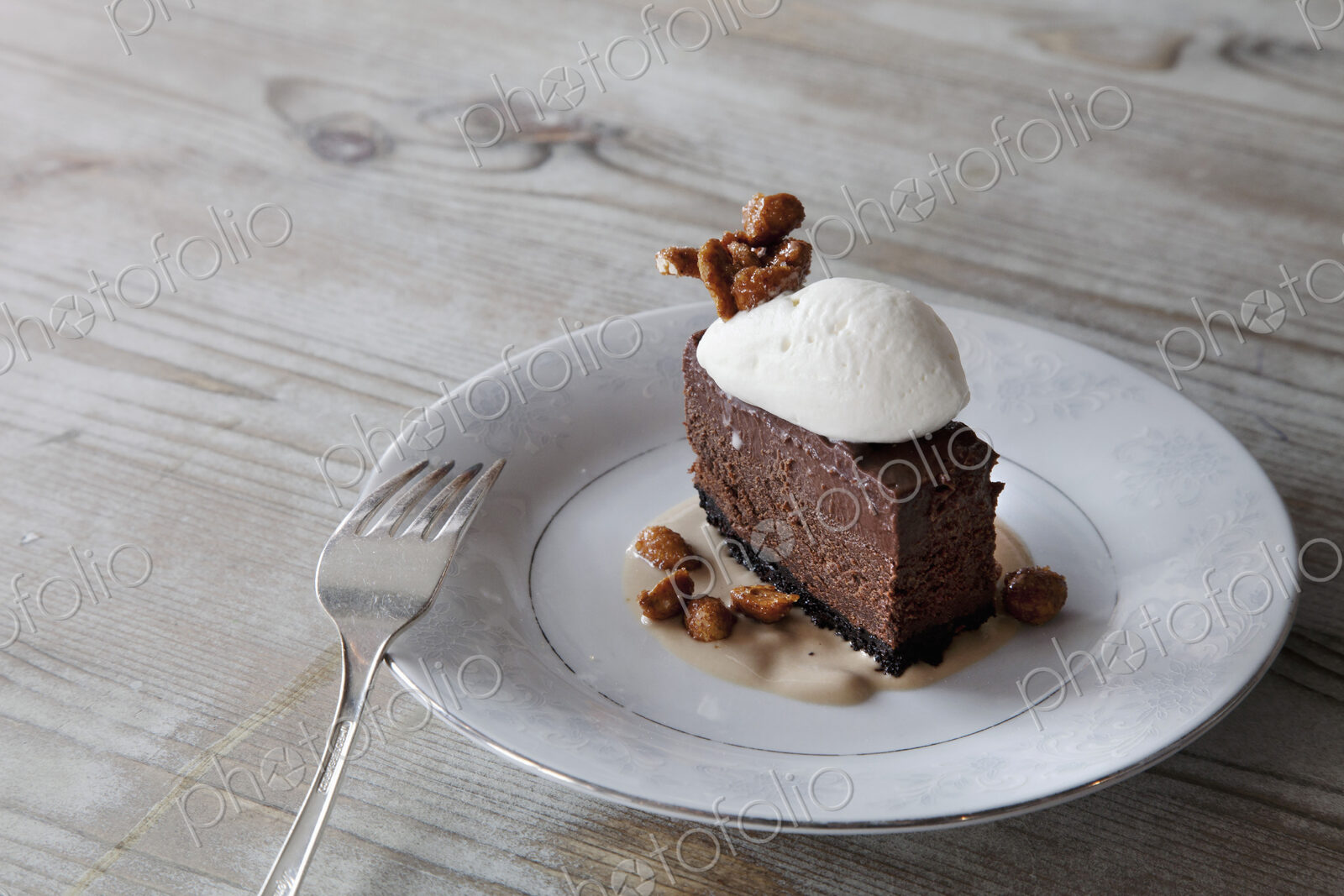 A slice of chocolate mousse dessert with ice cream, nuts nad sauce on a plate.