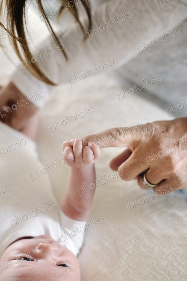 A small baby grasping his mother's finger.