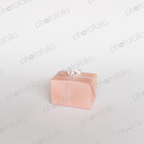 A small boxed gift wrapped in pink paper with a ribbon, on white background