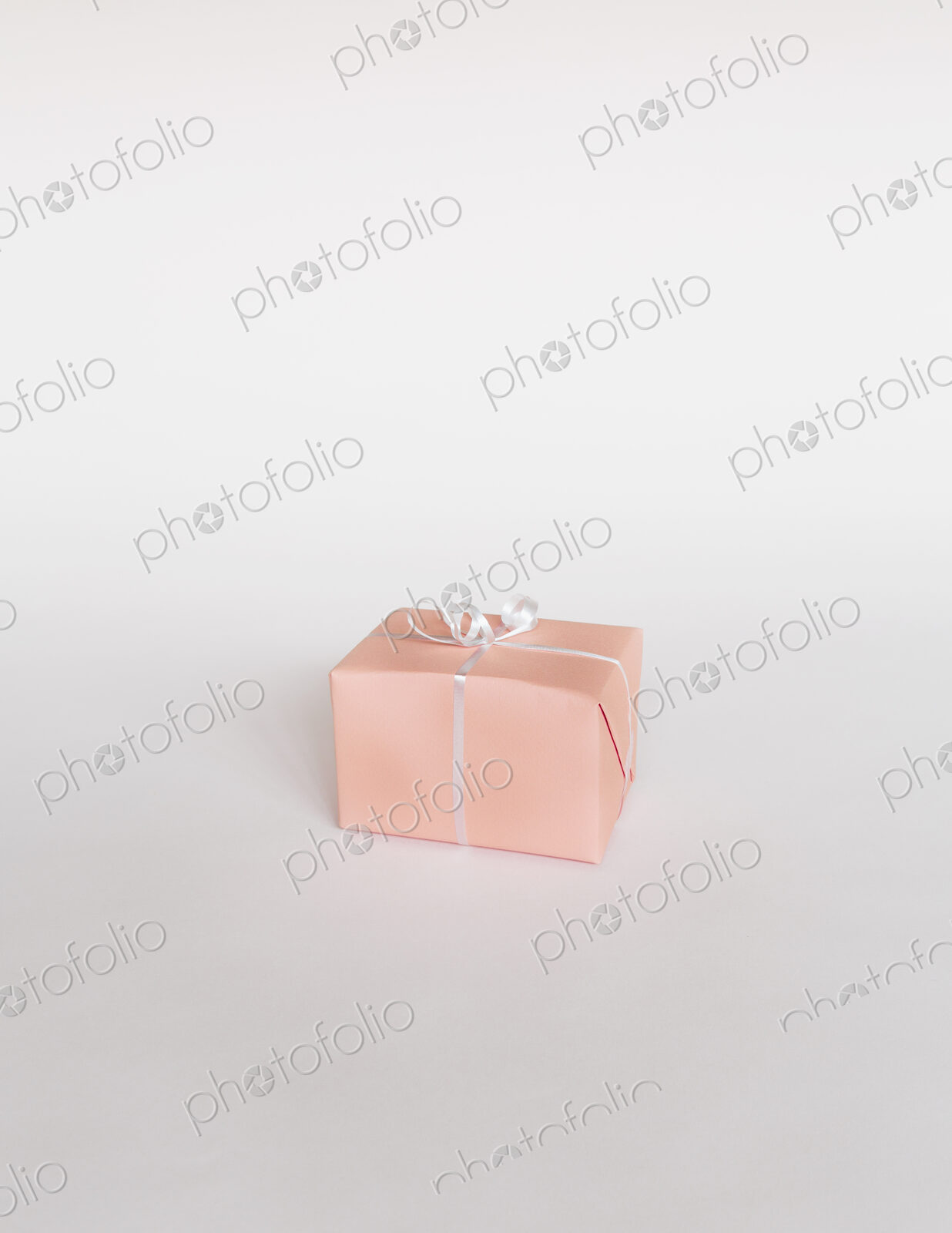 A small boxed gift wrapped in pink paper with a ribbon, on white background