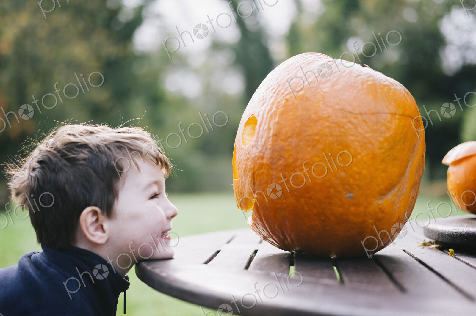 A small boy looking at a large pumpkin on a garden table.