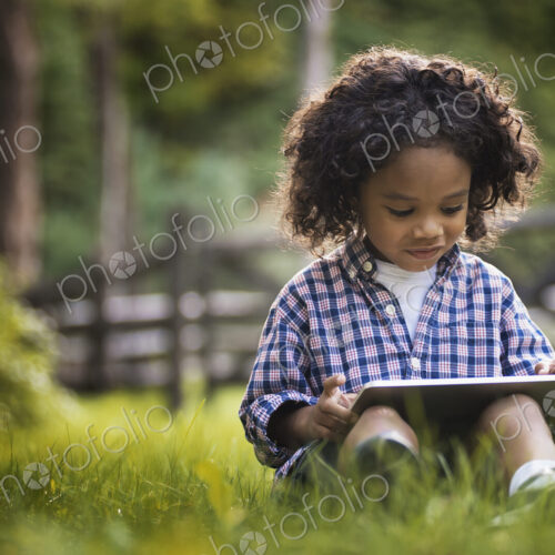 A small boy sitting on the grass using a tablet computer.