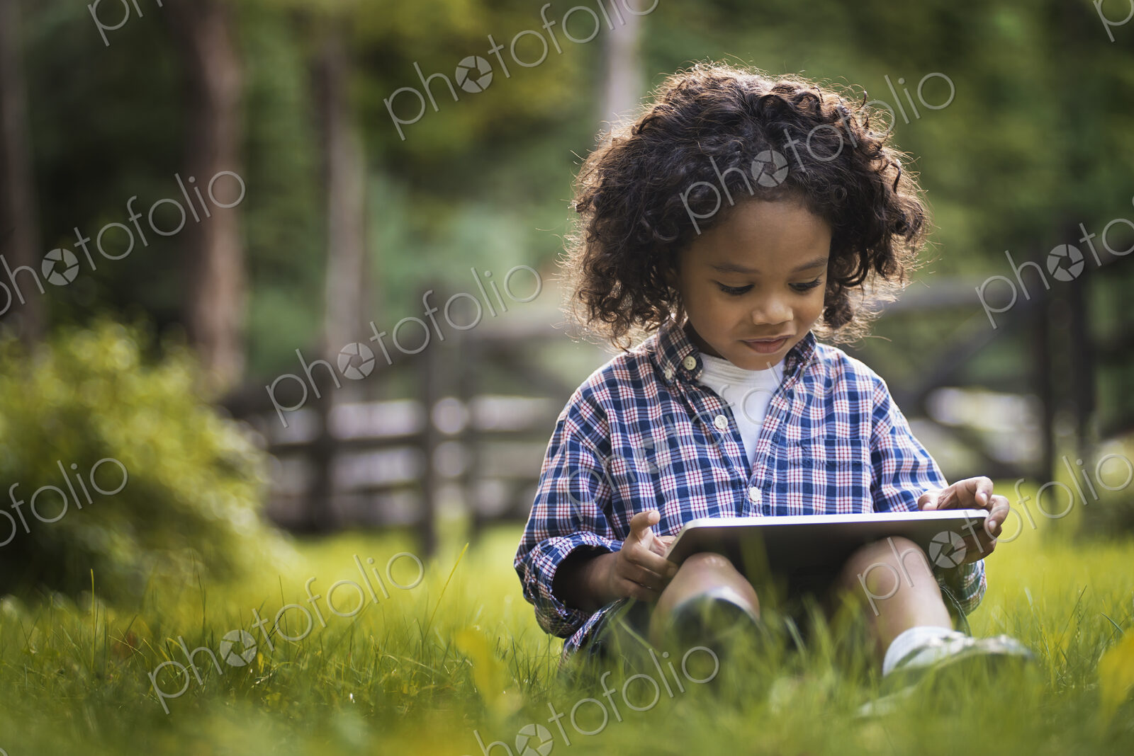 A small boy sitting on the grass using a tablet computer.