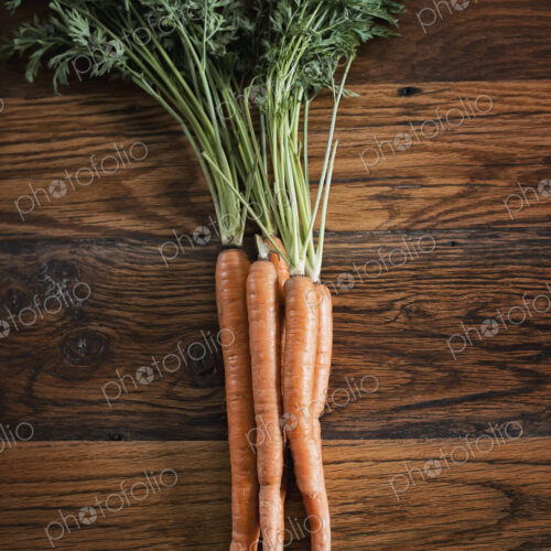 A small bunch of carrots with green leafy tops freshly harvested, lying on a tabletop.