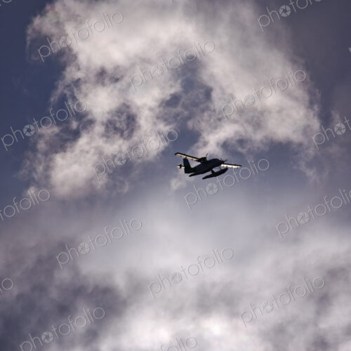 A small floatplane, a seaplane in the air in a sky full of clouds.