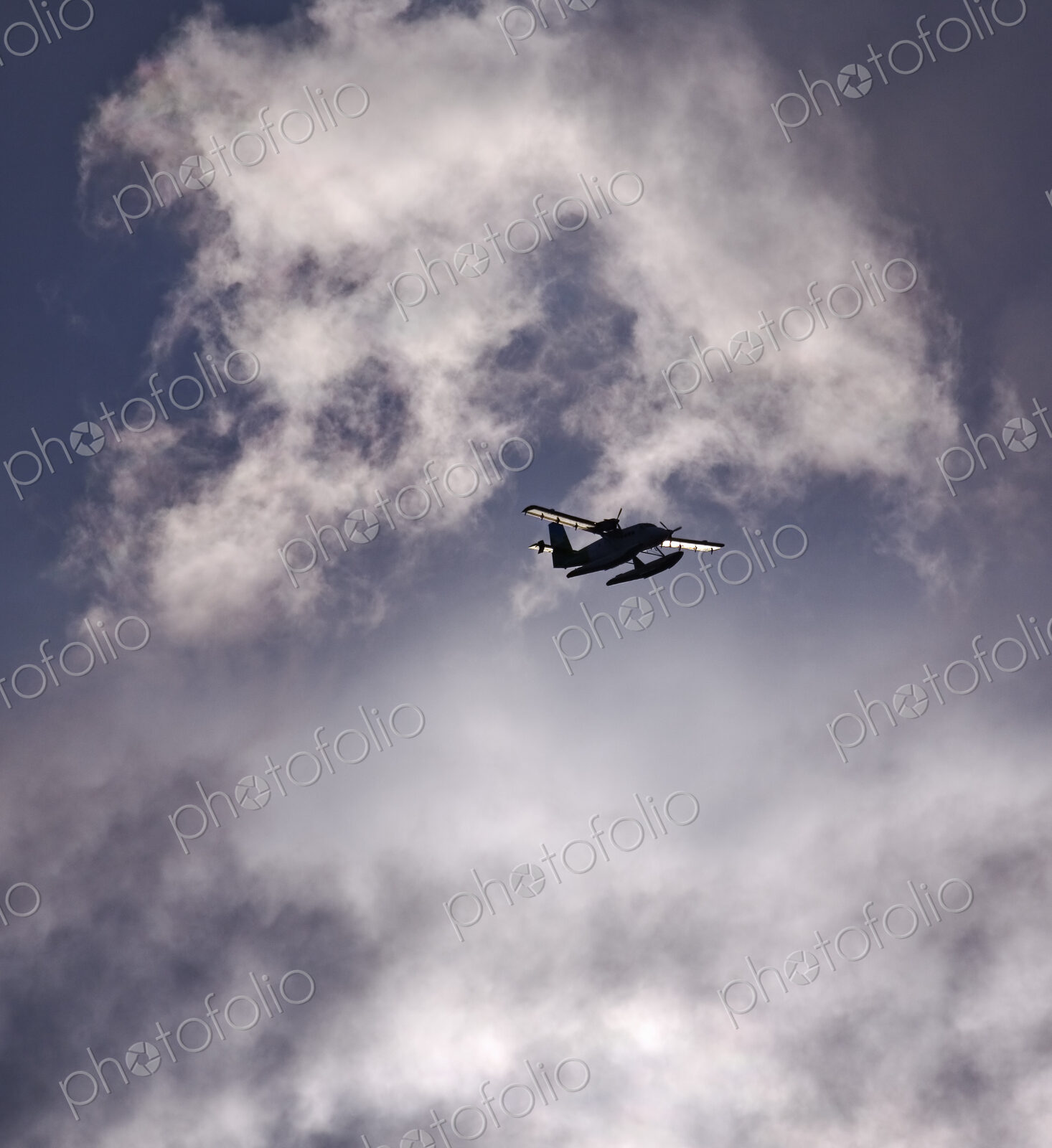 A small floatplane, a seaplane in the air in a sky full of clouds.