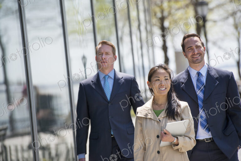 A small group of people, a businesswoman and two businessmen outdoors in the city.