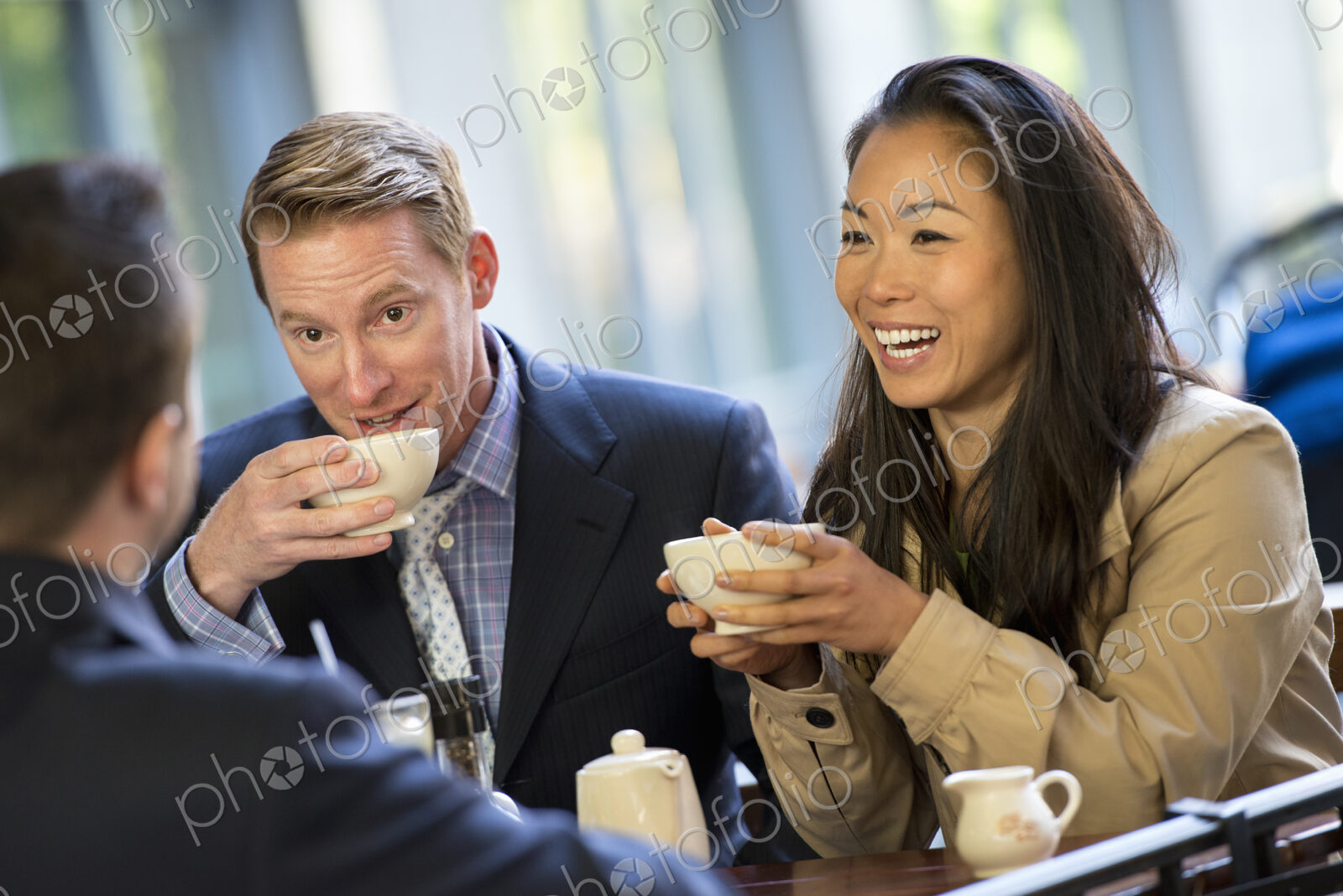 A small group of people, a businesswoman and two businessmen sitting in a coffee shop…