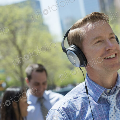 A small group of people outdoors in the city. A man listening to music on his… A small group of people outdoors in the city. A man listening to music on his…
