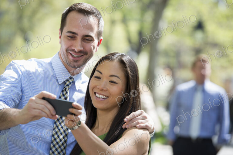 A small group of people. A couple with a smart phone, side by side. A man in the…