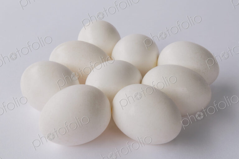 A small group or clutch of nine free range organic egg with white shells against a…