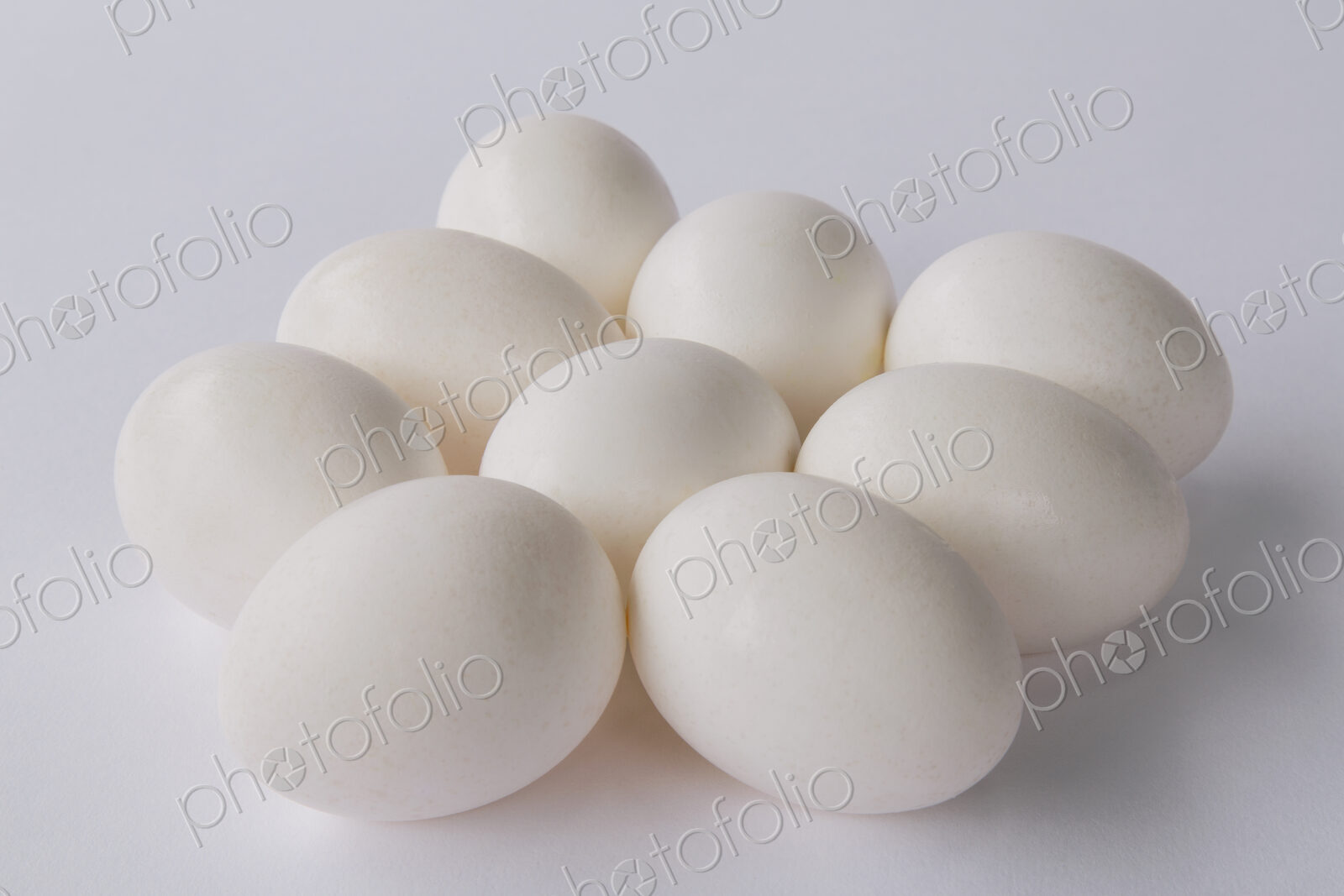 A small group or clutch of nine free range organic egg with white shells against a…