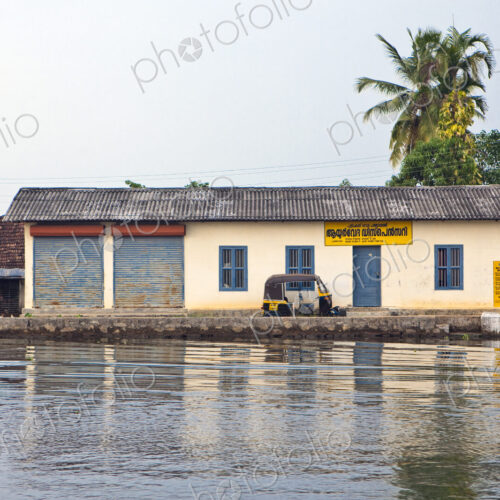 A small house by a waterway with a tuk tuk taxi in front, in the backwaters of Kerala,…