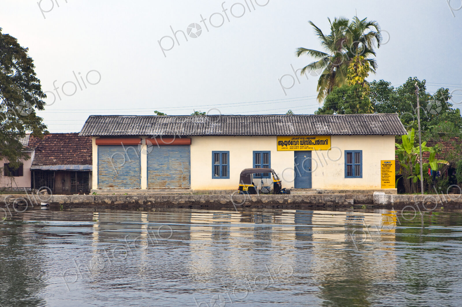A small house by a waterway with a tuk tuk taxi in front, in the backwaters of Kerala,…