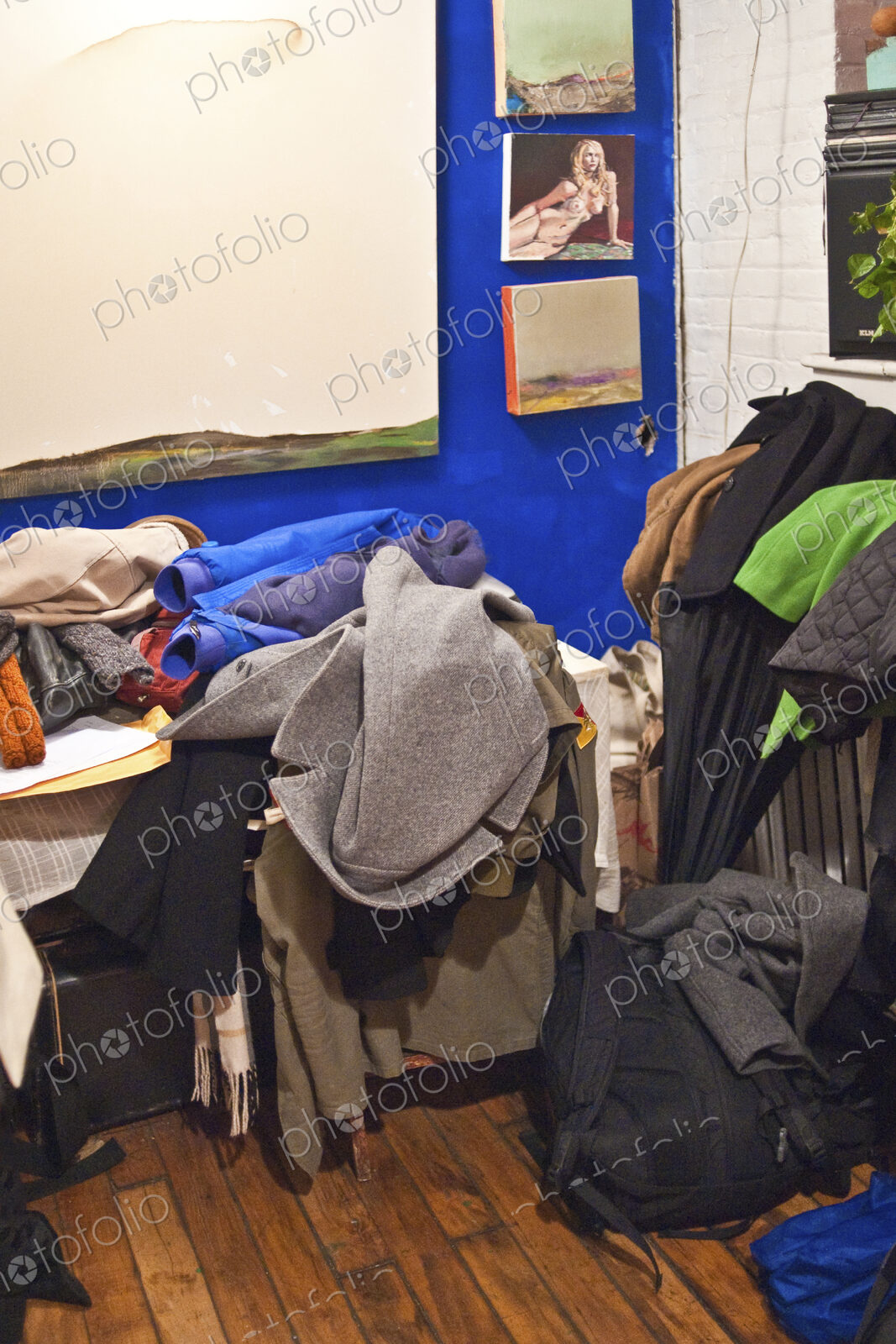 A small messy room with furniture covered in heaps of discarded clothes.