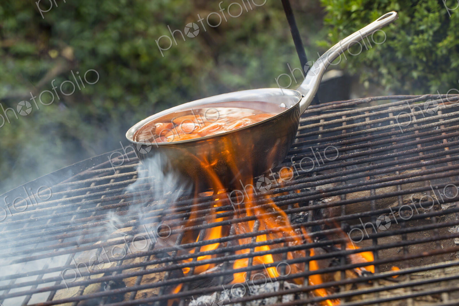 A small pan with sliced carrots over an open fire.