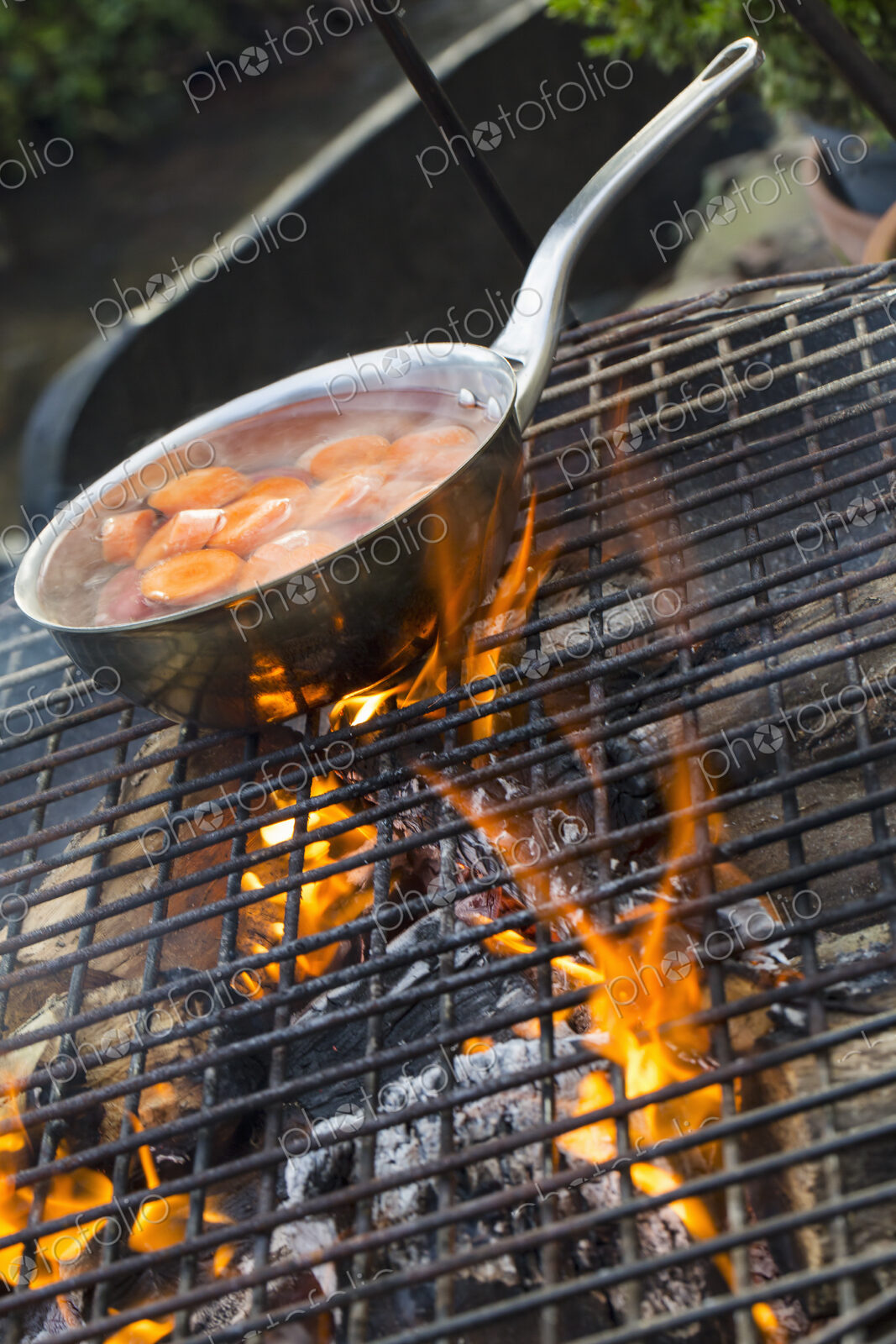A small pan with sliced carrots over an open fire.