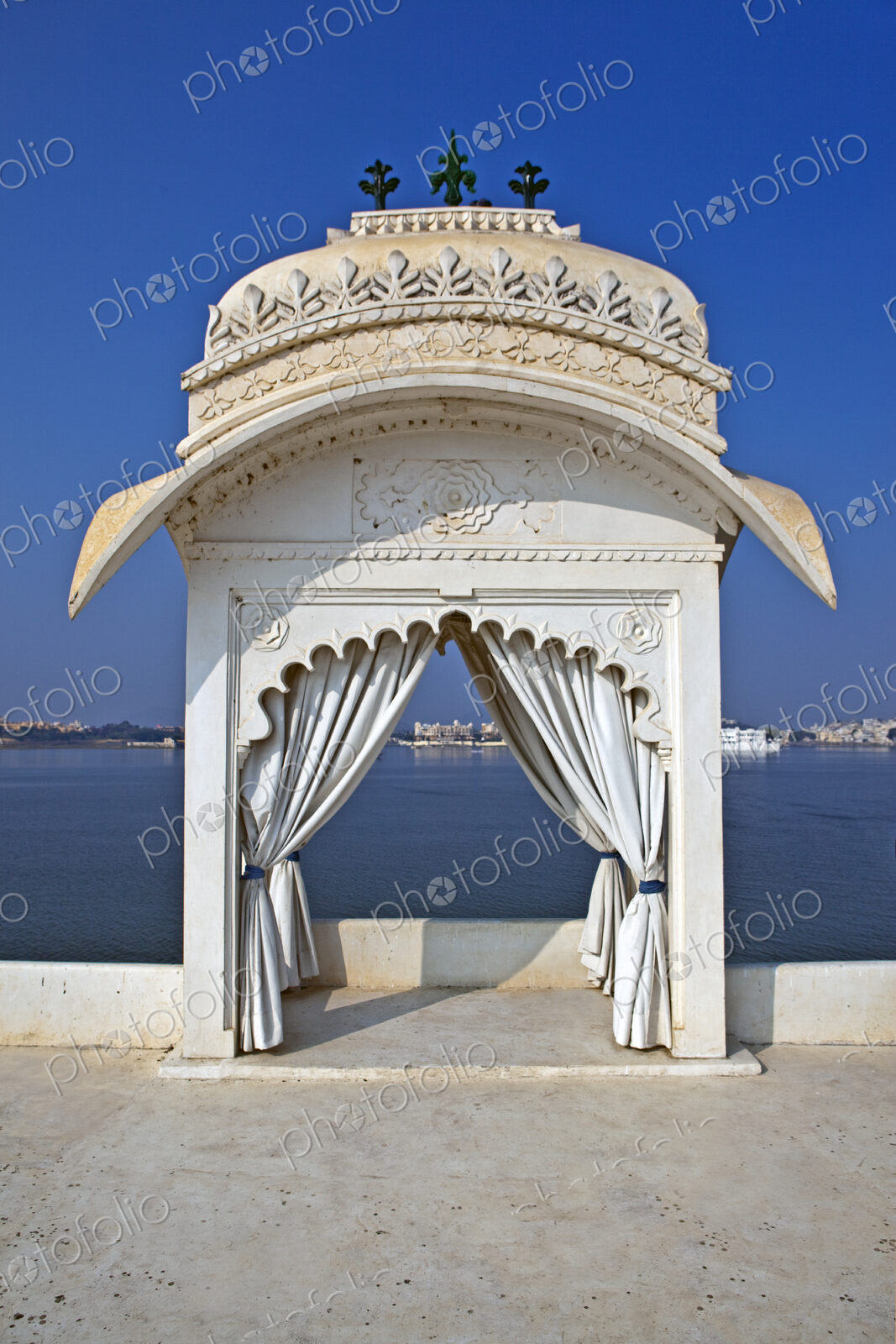 A small pavilion with a cupola, a scalloped carved stone arch with drapes drawn aside,…