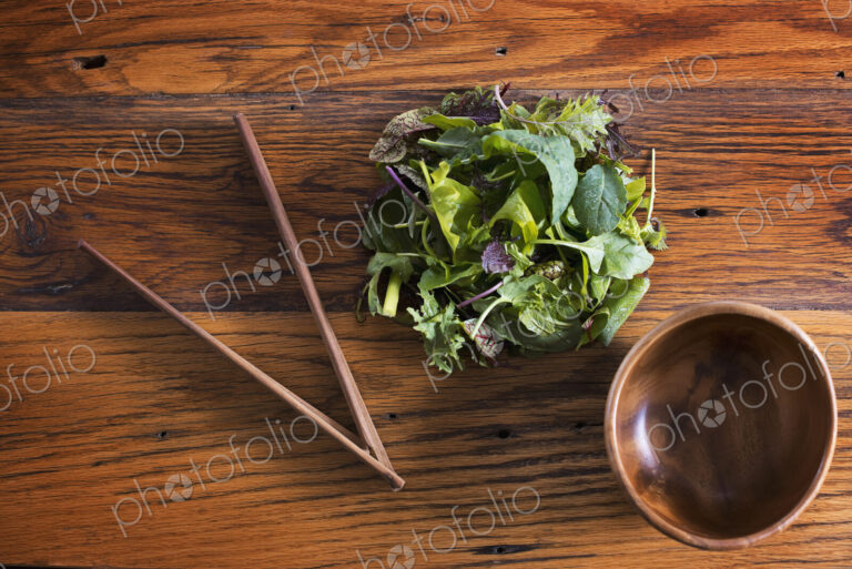A small round polished wooden bowl and a clutch of organic mixed salad leaves, with…