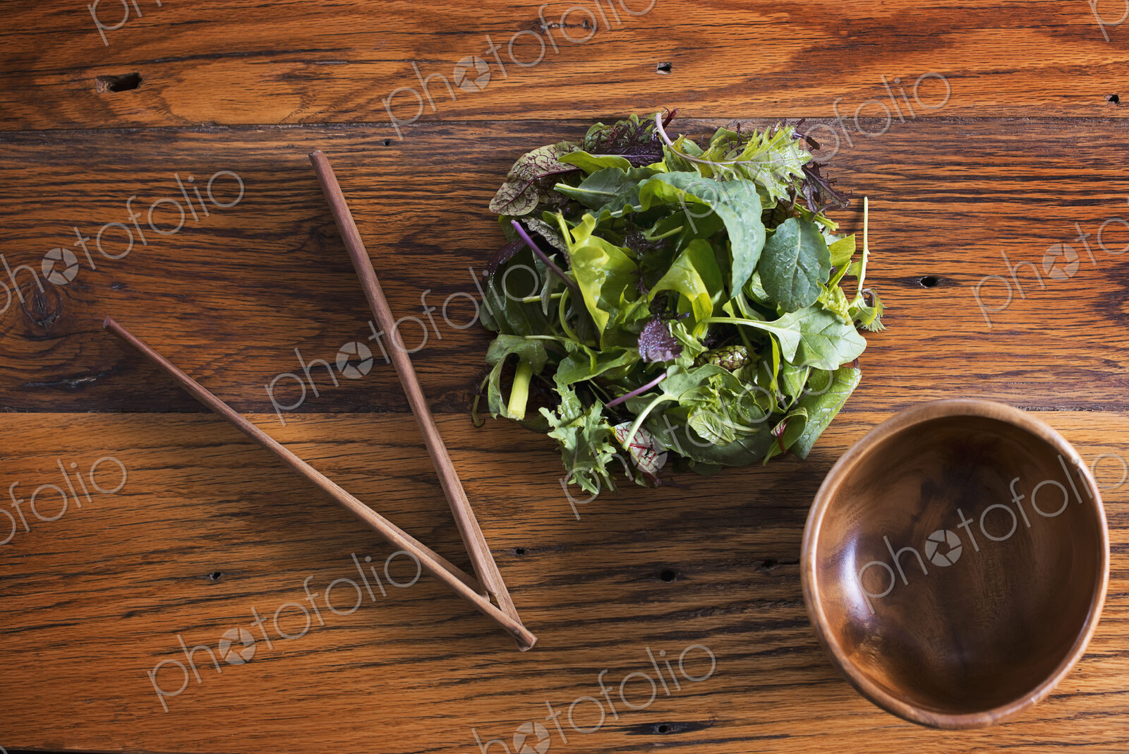 A small round polished wooden bowl and a clutch of organic mixed salad leaves, with…