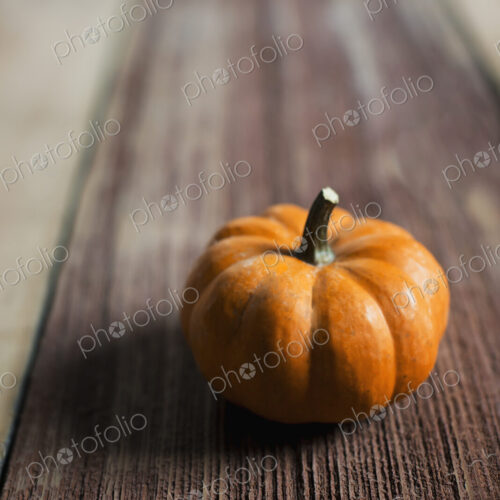 A small round pumpkin or squash vegetable with a bright orange skin, on a wooden tabletop.