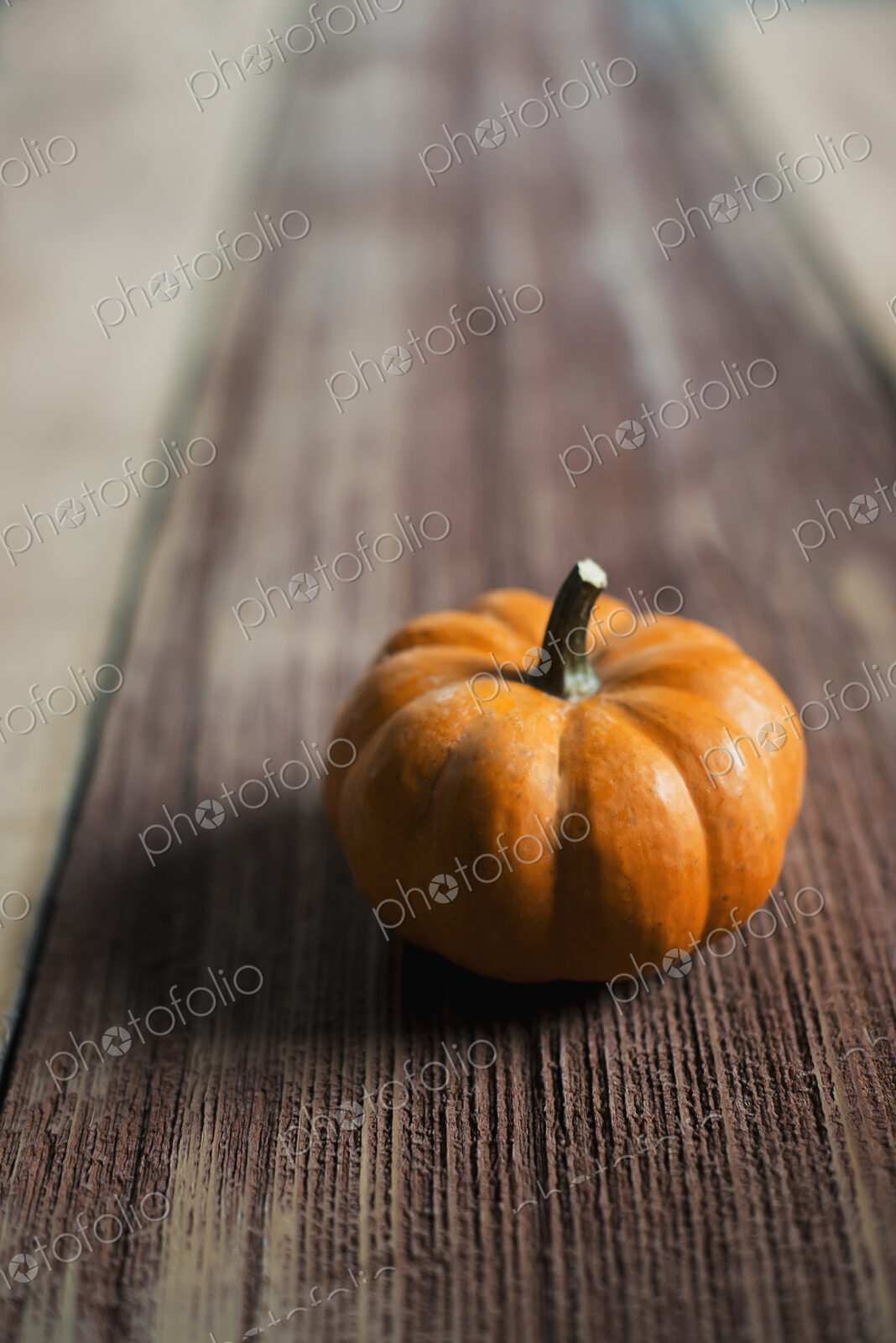 A small round pumpkin or squash vegetable with a bright orange skin, on a wooden tabletop.