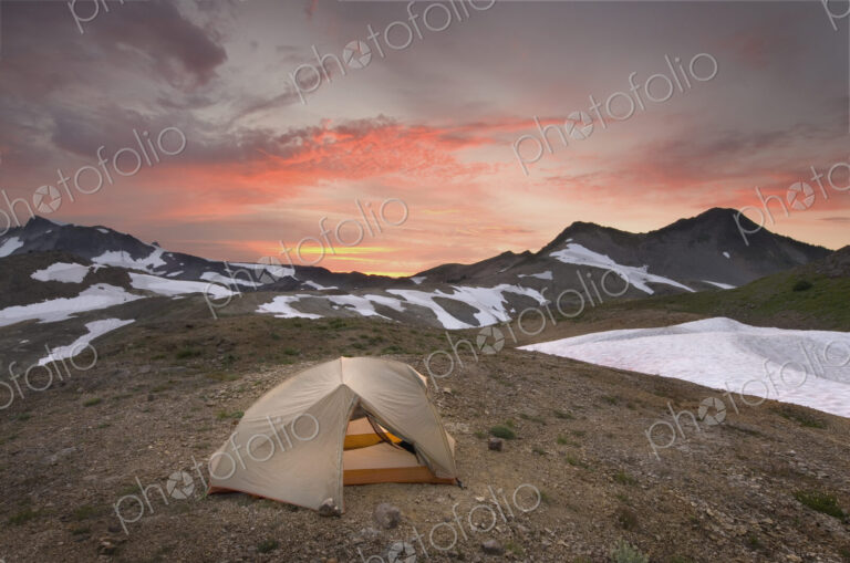 A small tent pitched on a screen slope just below the snowline, at sunset in the Mount…