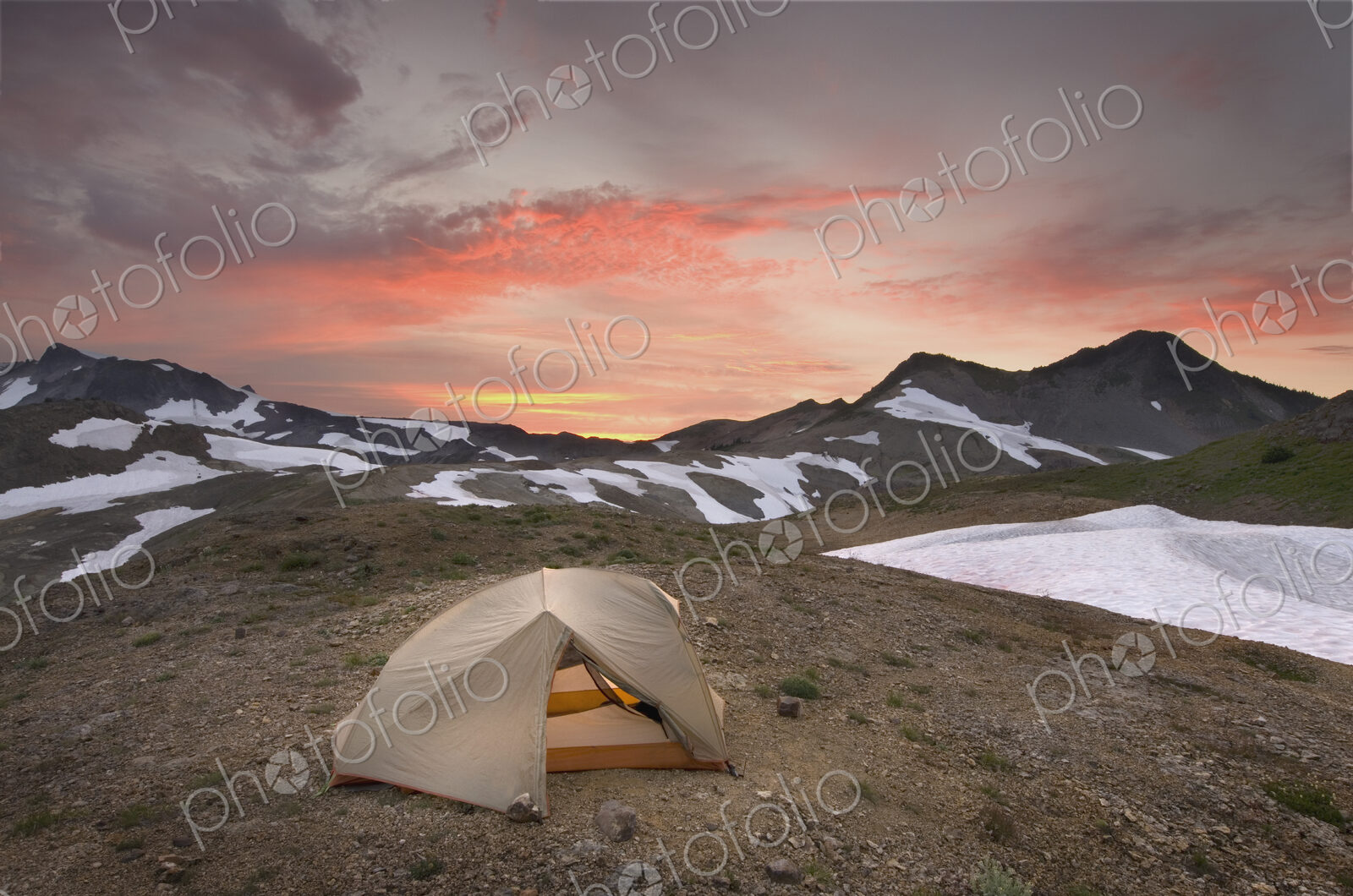 A small tent pitched on a screen slope just below the snowline, at sunset in the Mount…