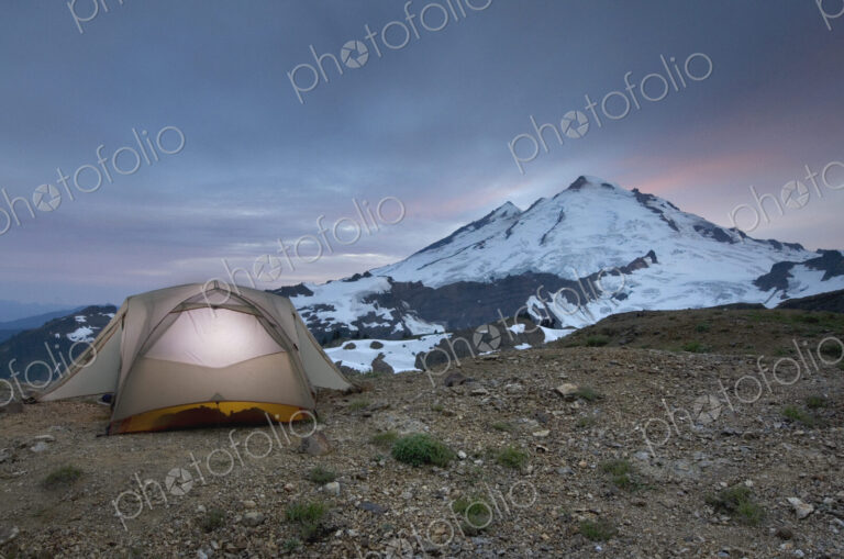 A small tent pitched on a screen slope just below the snowline, at sunset in the Mount…