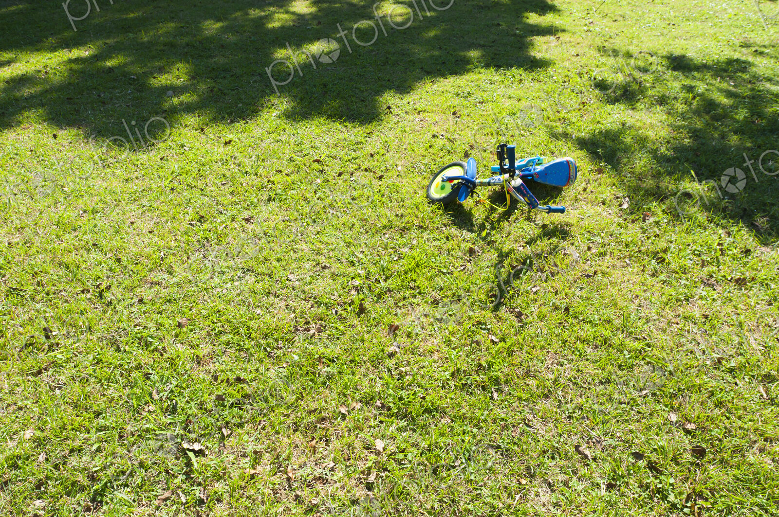 A small two wheeled decorated child’s bicycle on its side on the grass.