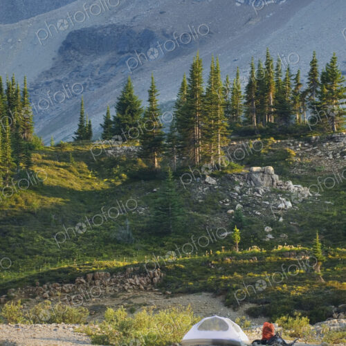 A small white tent and backpack on the shores of a lake in the Yoho National Park. A small white tent and backpack on the shores of a lake in the Yoho National Park.