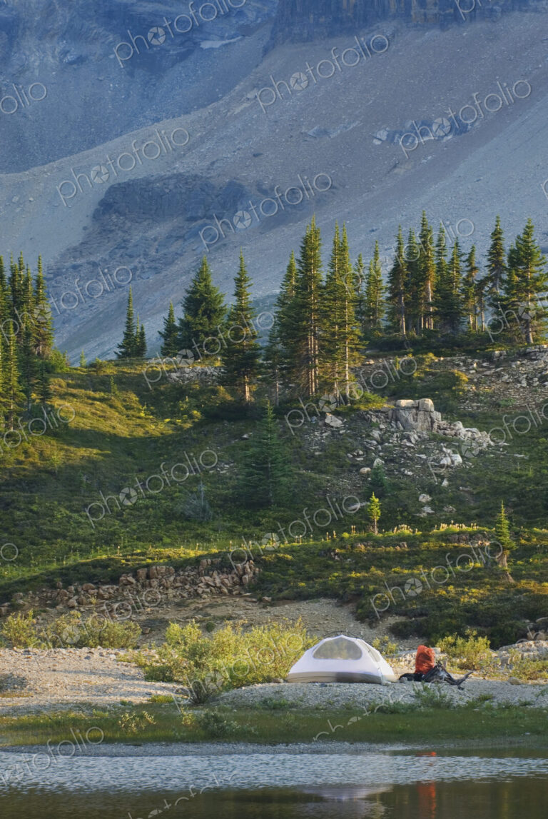 A small white tent and backpack on the shores of a lake in the Yoho National Park.