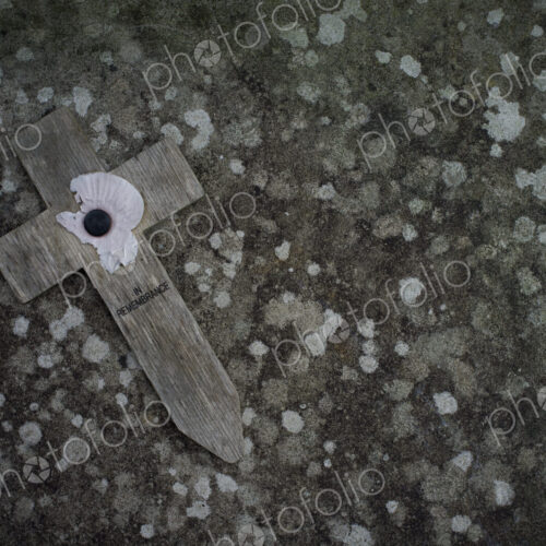 A small wooden cross with a poppy symbol commemorating the wartime dead, on a stone. A small wooden cross with a poppy symbol commemorating the wartime dead, on a stone.
